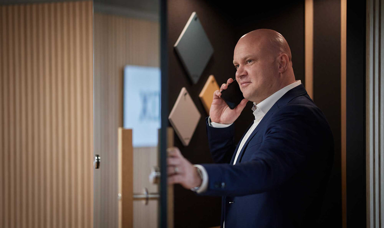 en person taler i telefonen, iført jakkesæt, i et moderne kontor med geometrisk kunst på væggen i baggrunden.